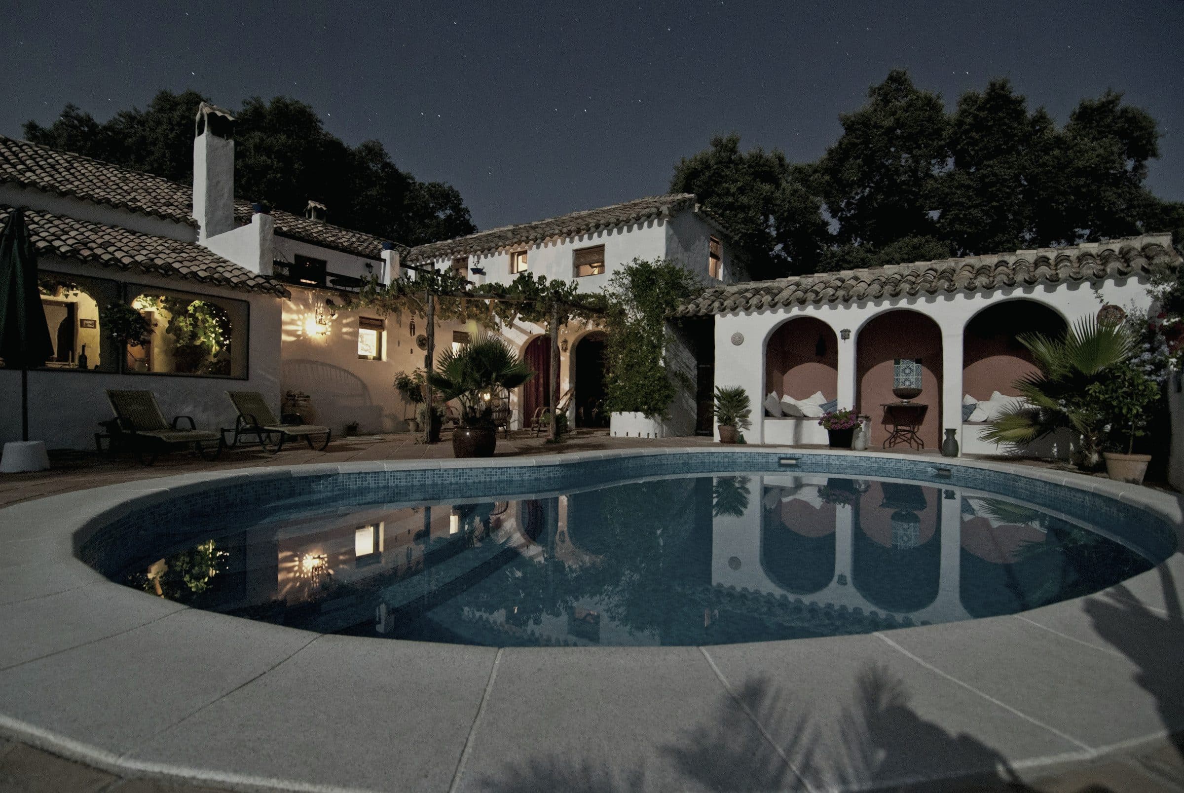 Masía mediterránea iluminada al anochecer, con la piscina reflejando la fachada