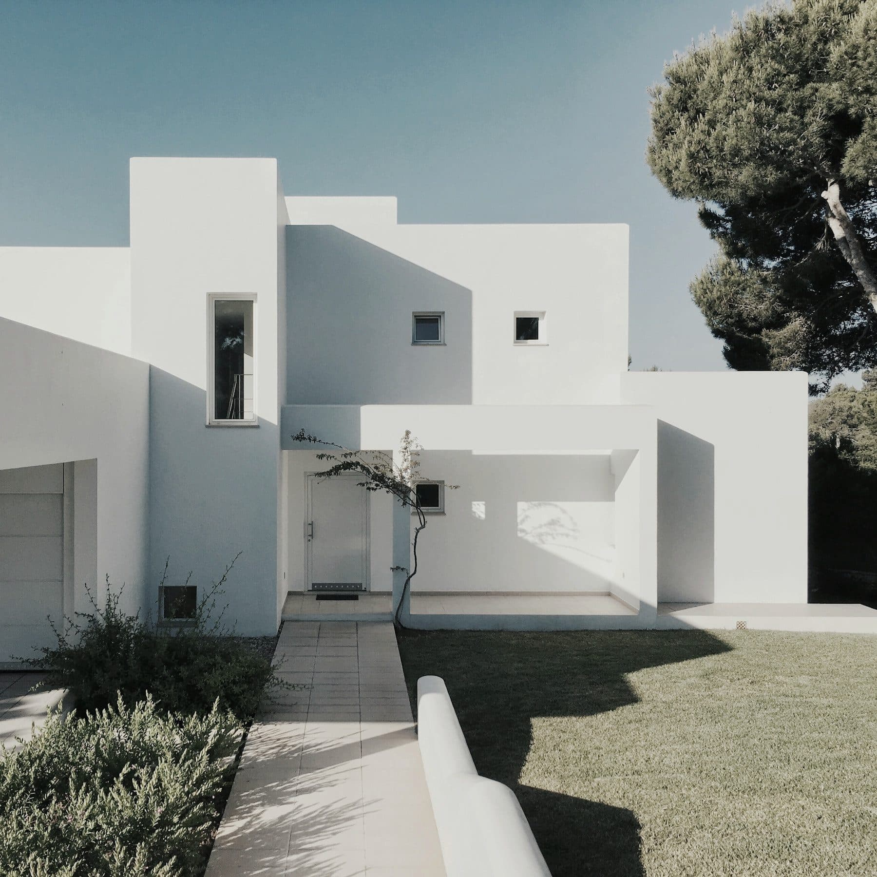 Villa mediterránea de líneas blancas bajo un pino piñonero